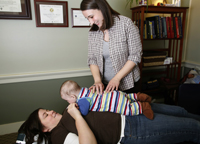 photo of female doctor touching the back of a baby who is lying on his mother's belly
